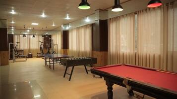 Mesa de billar, mesa de futbolín y mesa de ping pong en una habitación con ventanas amplias y cortinas.