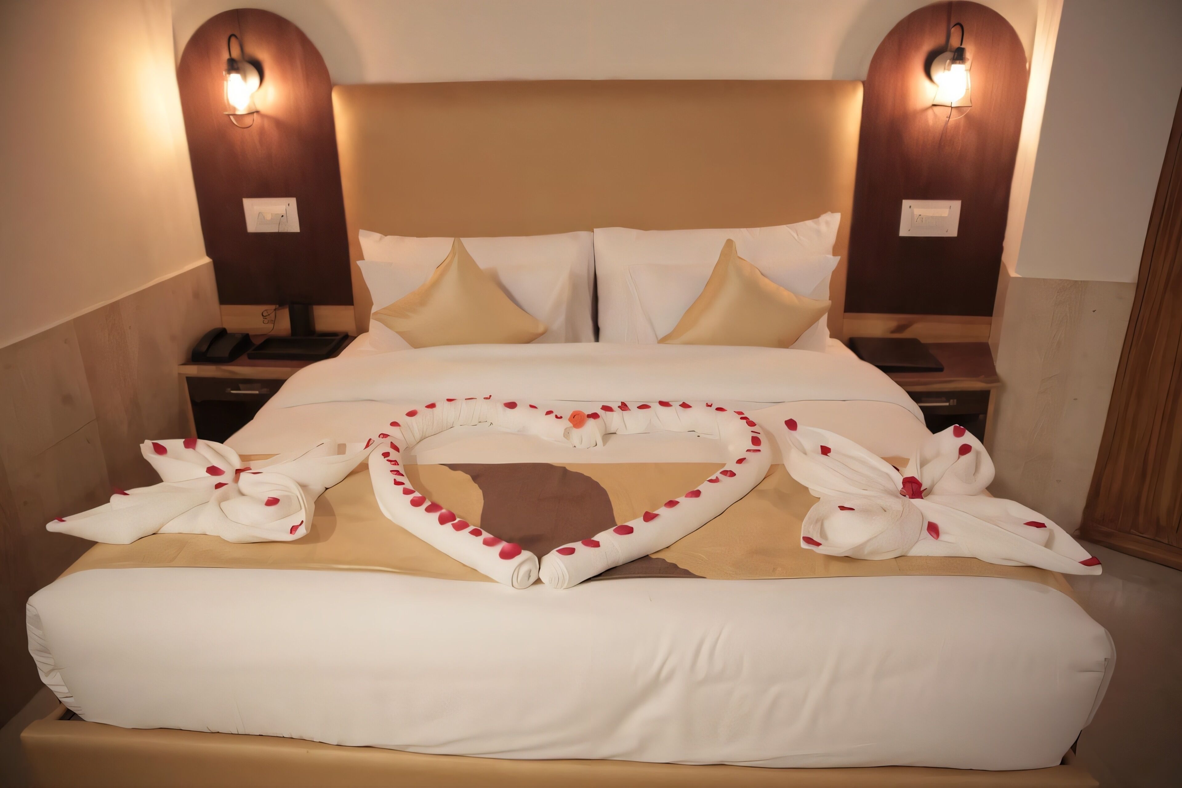 Una cama bien hecha con adornos con forma de corazón, dos lámparas de noche y un cabecero de madera.