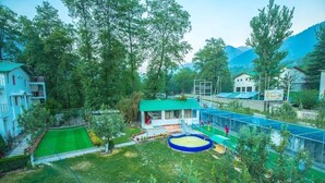Zona residencial con una casa, un área de juegos cercada y un césped verde.