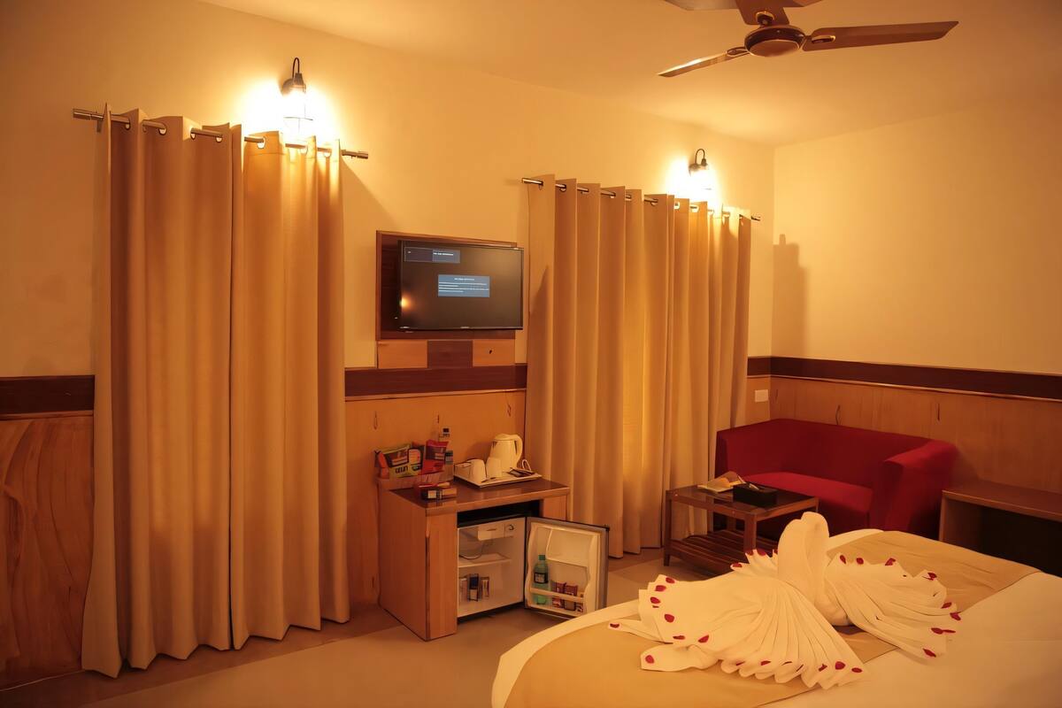 A hotel room with a bed, a red sofa, a TV, a desk with a mini-fridge, and curtains.