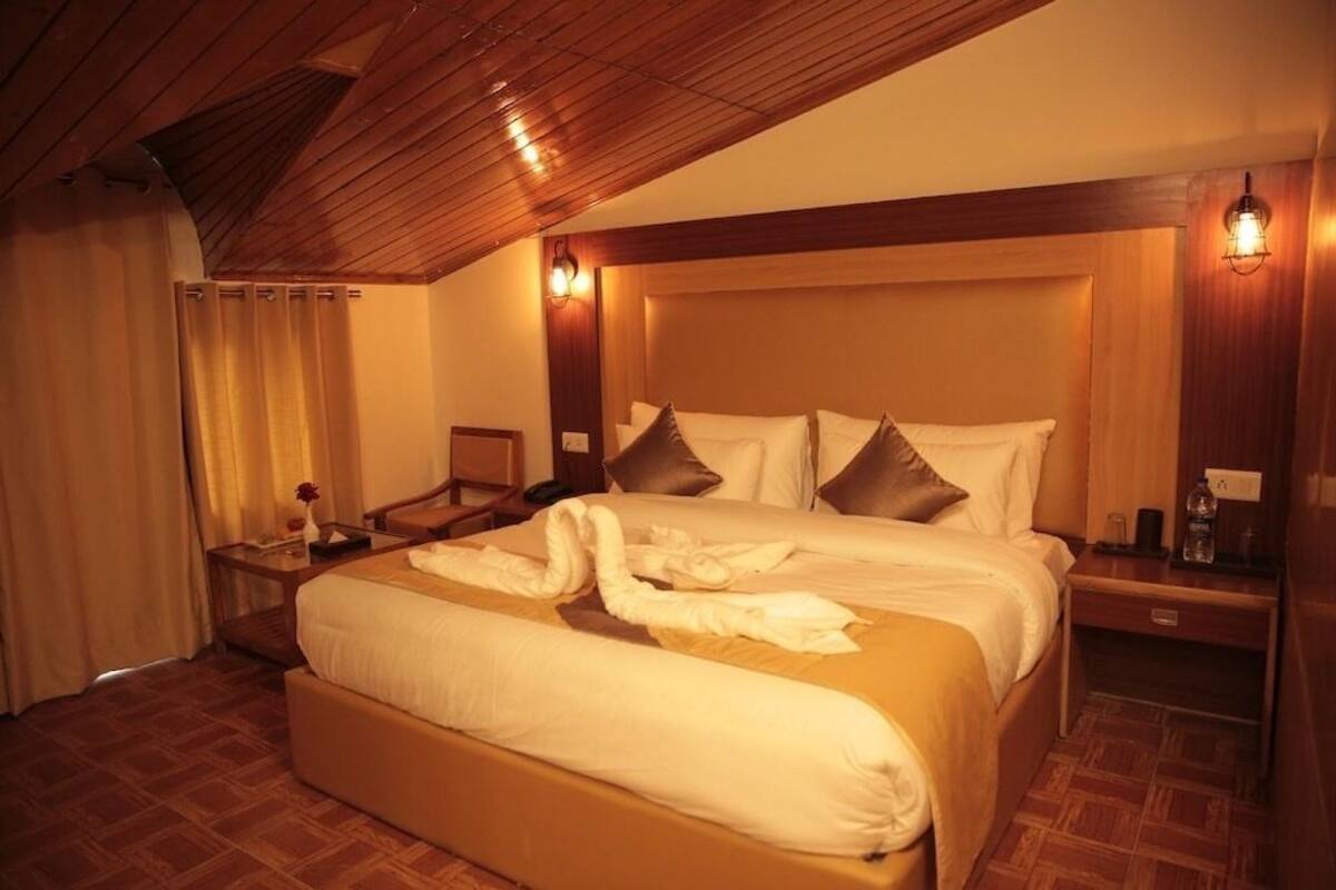 A hotel room with a large bed, wooden ceiling, and a nightstand with a lamp.
