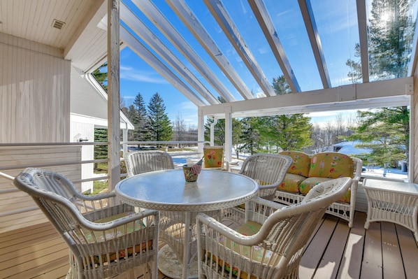 A covered outdoor seating area with wicker furniture and a table, overlooking a residential street.