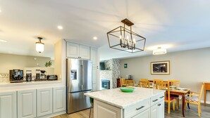 Una cocina moderna con armarios blancos, una isla grande, electrodomésticos de acero inoxidable y un comedor con sillas de madera.