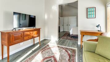 Un salon avec un téléviseur, un meuble en bois, un canapé vert et un tapis à motifs.