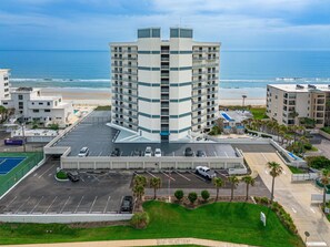 A multi-story hotel with a parking lot, a pool area, and a view of the beach.