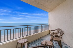 Een balkon met uitzicht op de oceaan, een hekwerk en twee stoelen.