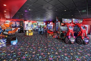 Une salle d’arcade intérieure comprenant divers jeux, un tapis à motifs et un plafond orné d’un motif quadrillé.