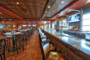 Un bar avec un long comptoir, plusieurs téléviseurs et un plafond décoré de motifs.