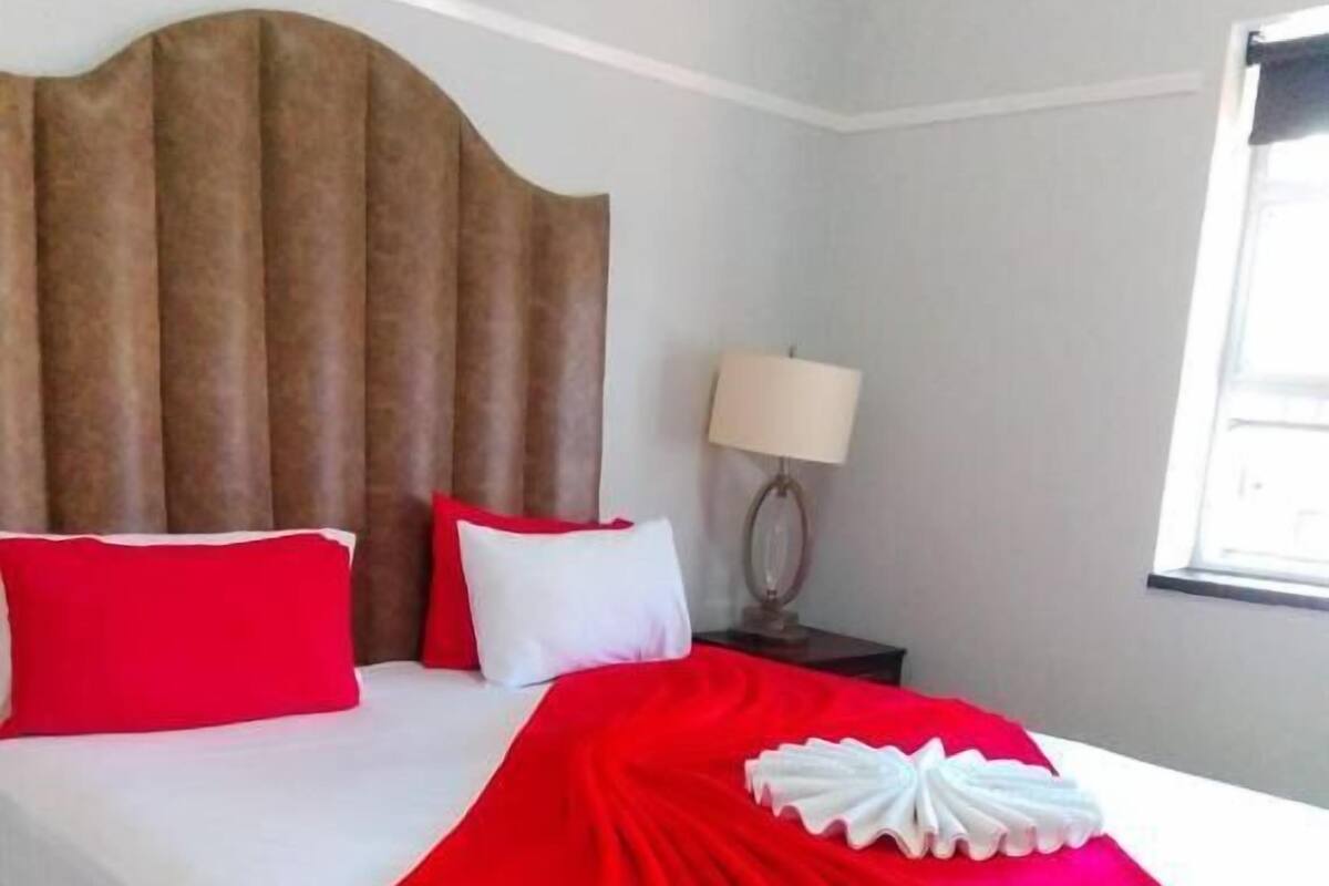 A hotel room with a large bed, a nightstand with a lamp, and a window.