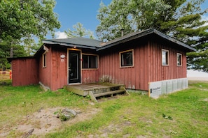 A small, single-story wooden cabin with a front door, a small porch, and a number '10' sign. - 3-Bedroom Cottage #10 (Nobel)