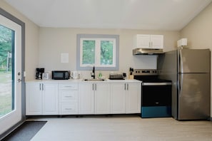 A modern kitchen with white cabinets, a stainless steel refrigerator, a microwave, and a stove. - 3-Bedroom Cottage #10 (Nobel)