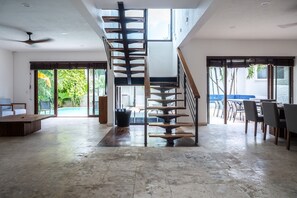 A spacious living area with a central staircase, a dining area with chairs and a table, and large windows offering views of greenery. - 5min walk to beach, housekeeping, pool at terrace, oceanview jacuzzi at rooftop (Playa del Carmen)
