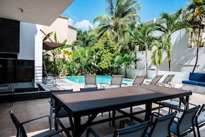 A poolside area with a dining table and chairs, a lounge area with a sofa, and a pool surrounded by palm trees. - 5min walk to beach, housekeeping, pool at terrace, oceanview jacuzzi at rooftop (Playa del Carmen)