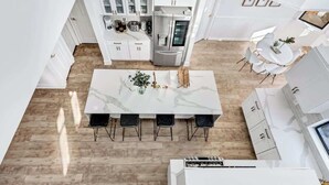 Cozinha moderna com armários brancos, bancada de mármore e área de jantar com mesa e cadeiras brancas.