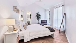 Quarto moderno com uma cama grande, mesas de cabeceira, ventoinha no teto e vista para o exterior.