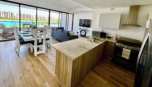 A modern kitchen with a large island, a dining area with a view, and a living room with a sofa and TV. - Urban Oasis- Modern comfort and stunning beach views (Punta Cana)