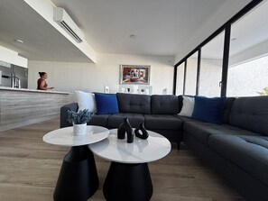 A modern living room with a sectional sofa, two round tables, and a kitchen area in the background. - Urban Oasis- Modern comfort and stunning beach views (Punta Cana)