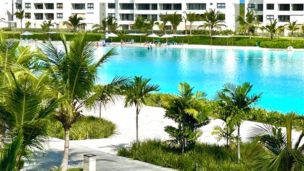 Ein Resort mit großem Schwimmbecken, Palmen und einem mehrstöckigen Gebäude mit Balkonen.
