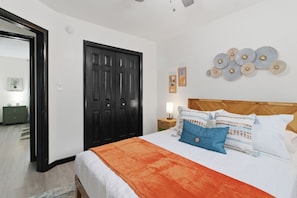 A bedroom with a bed, a nightstand, a dresser, a door, and wall art. - Sleeps 4, minutes from beach & Naval base (Norfolk)