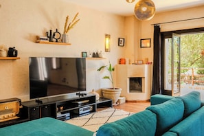 A living room with a large flat-screen TV, a fireplace, a sofa, and a potted plant.