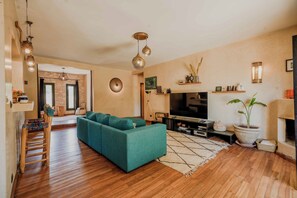 A living room with a teal sofa, wooden flooring, a flat-screen TV, and a fireplace.