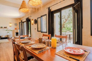 A dining area with a wooden table set for two, a glass of orange juice, and a view of the outdoors.