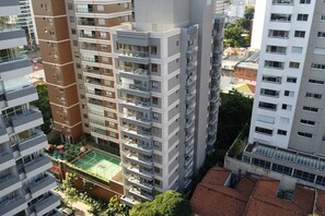 Un edificio residencial de gran altura con varios balcones, una terraza en la azotea y una cancha de tenis.
