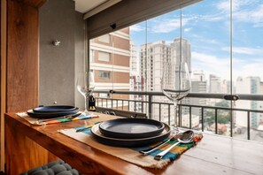 Una mesa de comedor con platos, cubiertos y un vaso en un balcón con vistas a la ciudad.