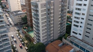 Un immeuble de grande hauteur doté de nombreux balcons, une rue bordée de voitures et des bâtiments adjacents.