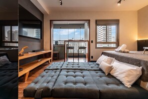 Quarto moderno com uma cama grande, um sofá, uma TV e uma varanda com vista para a cidade.