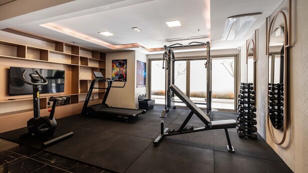 Une salle de sport moderne pour la maison, équipée de tapis de course, d’un support pour squats et d’haltères.