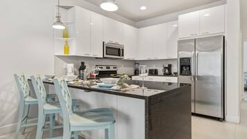 A modern kitchen with white cabinets, a stainless steel refrigerator, a microwave, and a central island with bar stools.