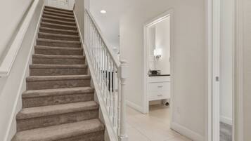 A carpeted staircase with white railings leading to a room with a white door and a small cabinet.