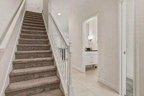 Ein Teppichstairlauf mit weißen Geländern führt zu einem Raum mit einer weißen Tür und einem kleinen Schrank.