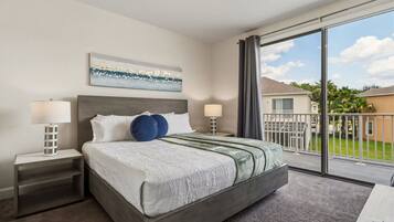 A hotel room with a large bed, two bedside tables, a window with a view of a residential area, and a painting on the wall.
