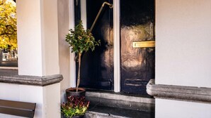 Een zwarte deur met een koperen handgreep, een bloempot en een klein bankje buiten.