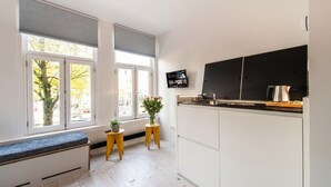 Een moderne keuken met witte kastjes, een zwart aanrechtblad en een inbouwoven. Er staan twee kleine houten krukjes en een potplant.