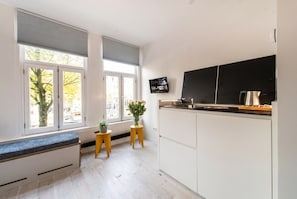 Eine moderne Küche mit weißen Schränken, einer schwarzen Arbeitsplatte und einem eingebauten Backofen. Zwei kleine Holzschemeln und ein Blumentopf sind ebenfalls vorhanden.
