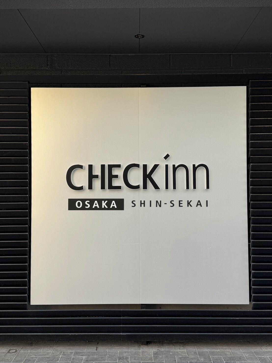 A large, white sign with the text 'CHECKINN OSAKA SHIN-SEKAI' in black.