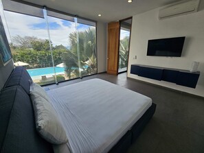 Une chambre moderne avec un grand lit, un téléviseur fixé au mur et une vue sur une piscine.