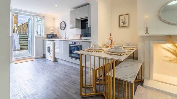 A modern kitchen with a dining area, a washing machine, and a fireplace. - Tide & Seek — Garden Flat by the Sea (Walmer)