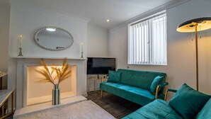 A living room with a fireplace, a sofa, a TV, and a floor lamp. - Tide & Seek — Garden Flat by the Sea (Walmer)