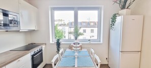 Eine Küche mit Fenster, einem Esstisch mit Stühlen, einem Kühlschrank und einer Mikrowelle.