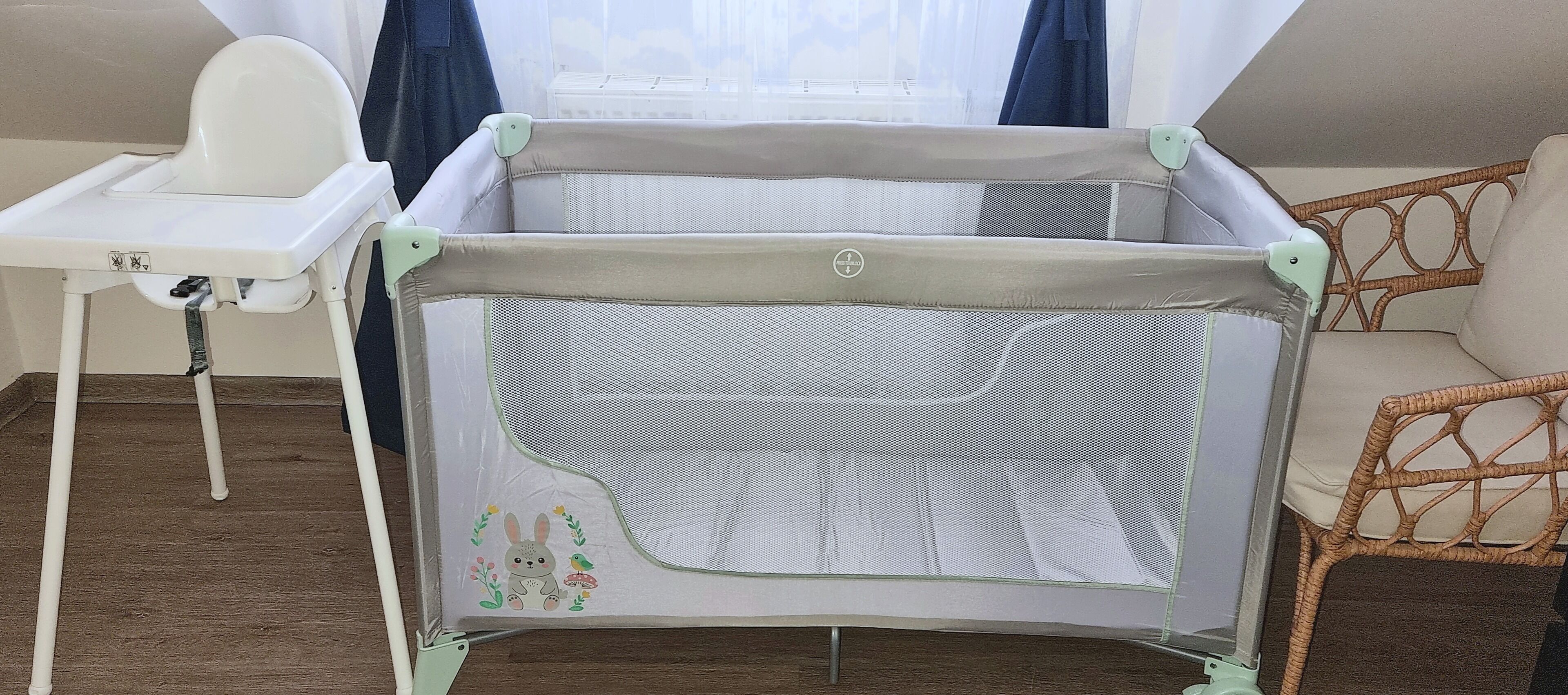 Een babyren met een gaasje voor, een witte kinderstoel en een rieten stoel.