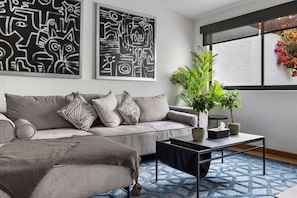 A modern living room with a grey sofa, patterned cushions, a coffee table, and two abstract wall art pieces.