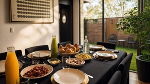 Una mesa de desayuno servida con diferentes platos, una botella de jugo y una cesta de cruasanes.