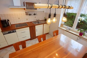Una cocina con mesa de madera, armarios blancos, horno empotrado y lámparas colgantes.