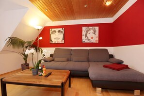A modern living room with a brown sofa, a wooden coffee table, and two wall-mounted paintings. - Spacious Apartment – Private Covered Terrace, Garden, Playground Nearby (Villingen-Schwenningen)