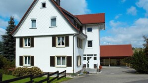A two-story building with a red roof, multiple windows, and a front entrance. - Spacious Apartment – Private Covered Terrace, Garden, Playground Nearby (Villingen-Schwenningen)