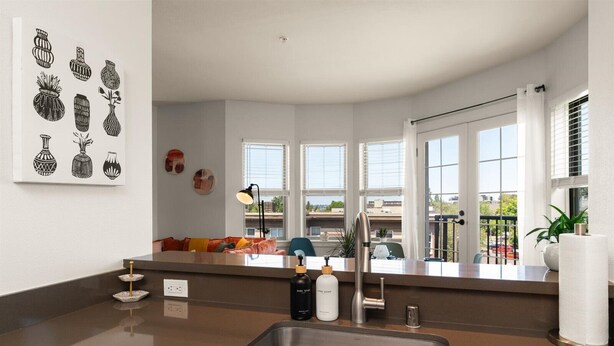 Eine moderne Küche mit Spüle aus Edelstahl, einer Arbeitsplatte mit Handseifenflasche und einem Fenster mit Blick auf einen Balkon.